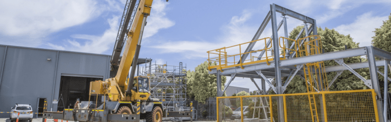 C1 Crane Ticket Perth - Slewing Mobile Crane in Operation at a a warehouse facility with scaffolding structure in the background.