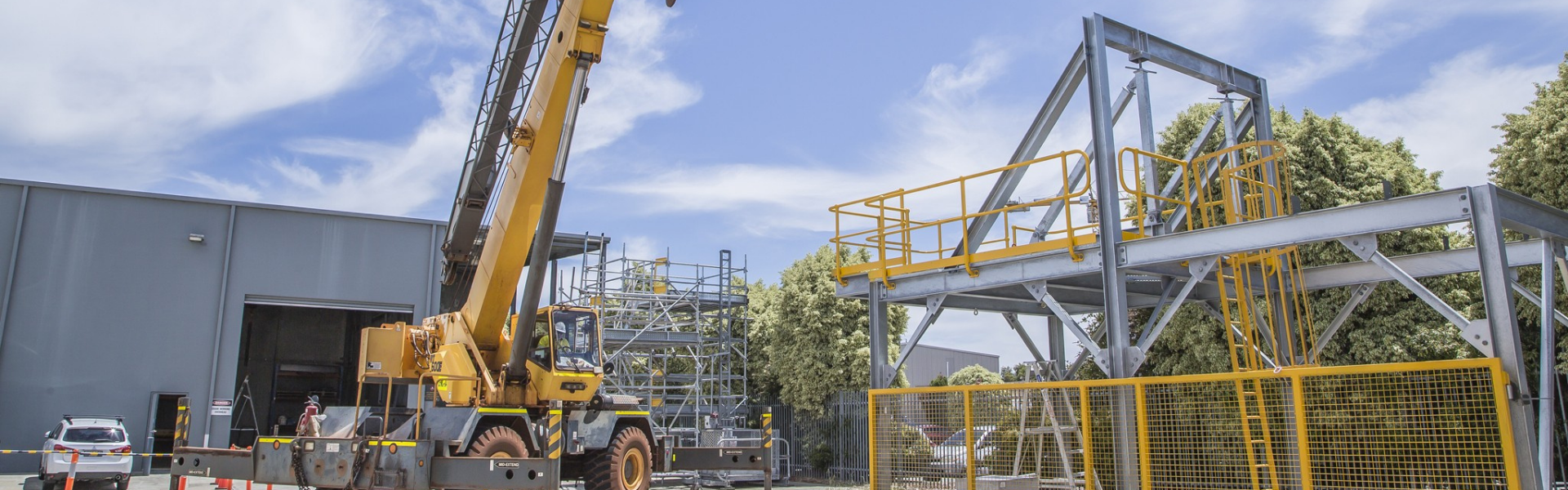 C1 Crane Ticket Perth - Slewing Mobile Crane in Operation at a a warehouse facility with scaffolding structure in the background.