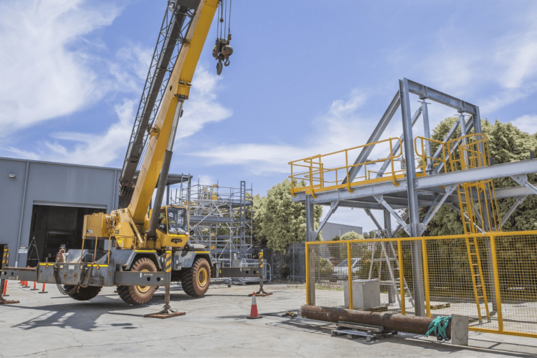 C1 Crane Ticket Perth - Slewing Mobile Crane in Operation at a warehouse facility with scaffolding structure in the background.