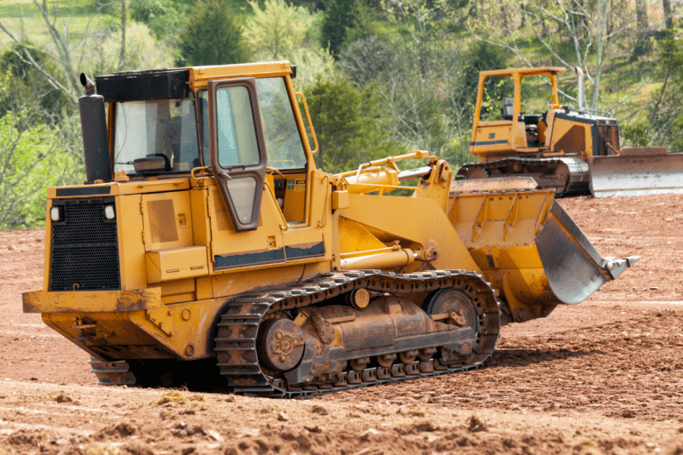 Conduct Civil Construction Dozer Operations. Two yellow bulldozers operating on a construction site with greenery in the background
