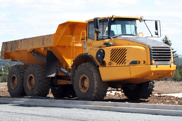 Conduct Articulated Dump Truck Operations / Dump Truck Training Perth WA. Bright yellow articulated dump truck on an industrial yard with construction equipment in the background. Dump Truck Ticket Training