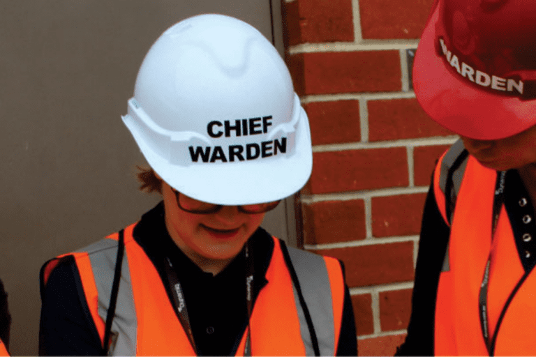 Young female chief fire warden wearing HiVis vest talking to a worker.