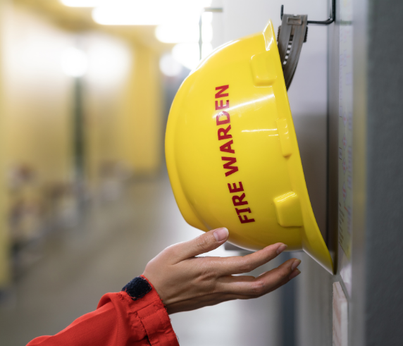 Hand touching the underside of a yellow hard hat that's labeled fire warden.
