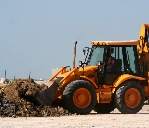 Front end loader being used to excavate large mound of dirt in a industrial site.