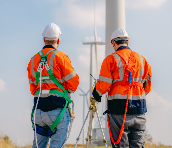 Two heights safety supervisors supervising a working wind farm turbine with a large white wind turbine in the background.