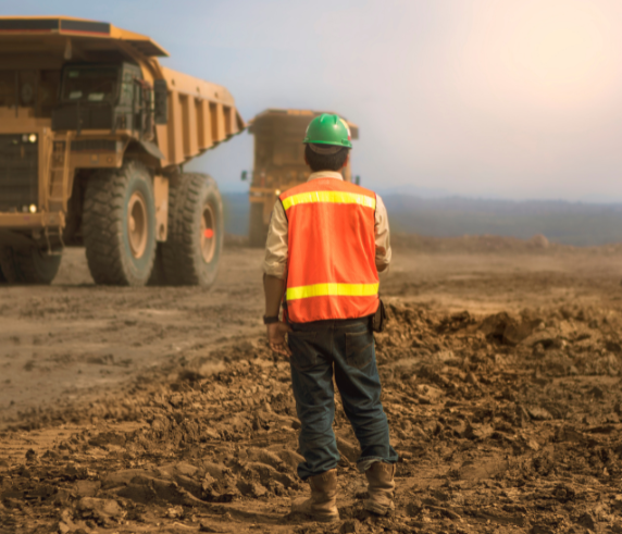 Statutory Supervisor wearing PPE standing in moved earth looking at Articulated haul dump truck.
