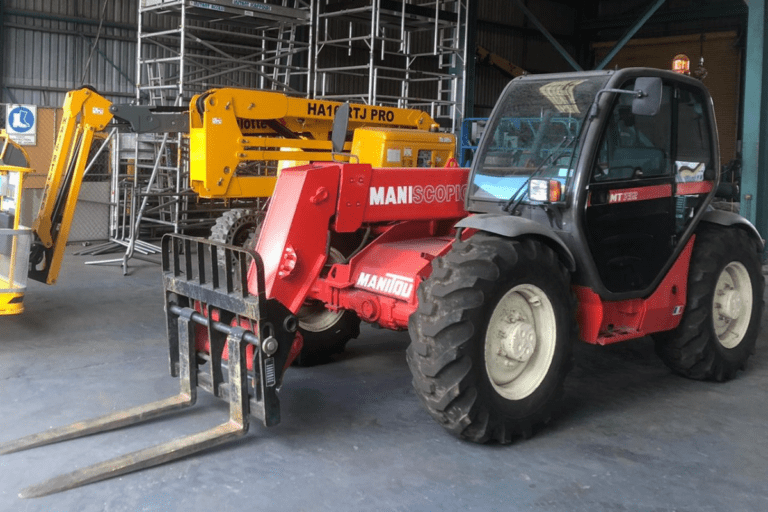 Conduct Telescopic Materials Handler Operations. A telescopic materials handler positioned on a training course site with industrial structures in the background