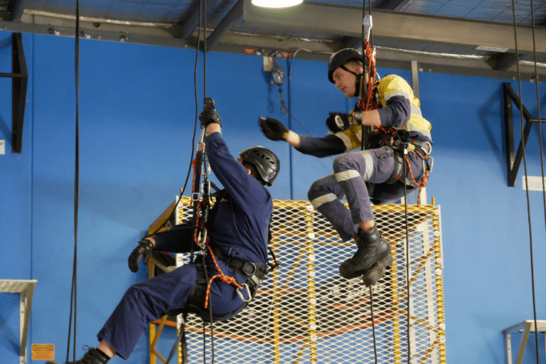 Two trainees harnessed and suspended from a warehouse ceiling participating in Saferight's Working Safely From Heights course delivered at Saferights training facility.