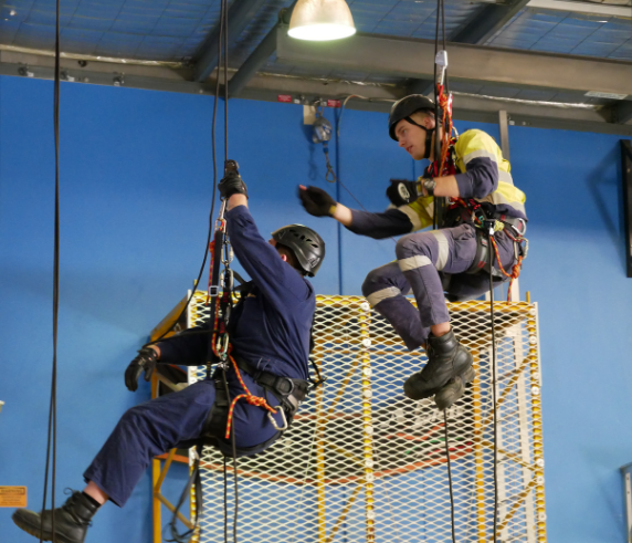 Two trainees harnessed and suspended from a warehouse ceiling participating in Saferight's Working Safely From Heights course delivered at Saferights training facility.
