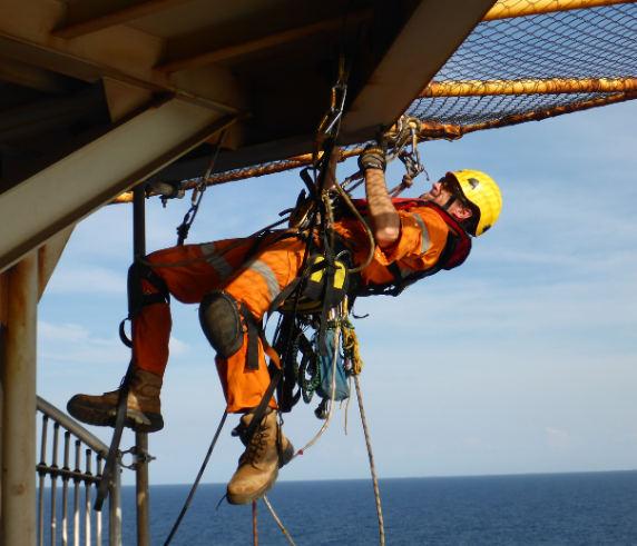 Worker Hitched onto oil rig structure hanging upside down above the ocean performing Work Safety From Heights.