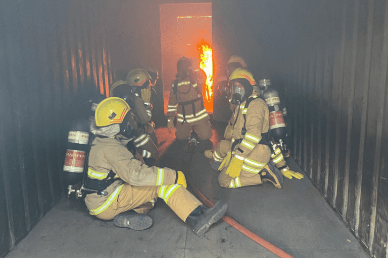 Firefighting trainees in full gear operating breathing apparatus during a live fire training exercise at Saferight Welshpool facility