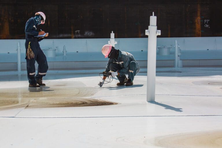 Two male worker inspection visual roof deck plate storage tank oil one is kneeling down the other is standing near him.