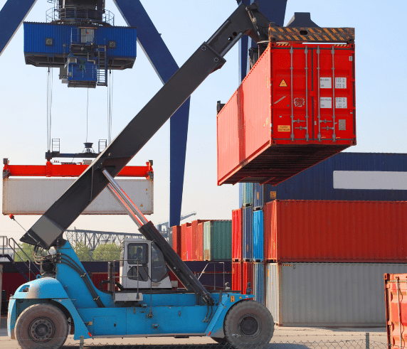 A reach stacker lifting a red cargo container at a container terminal