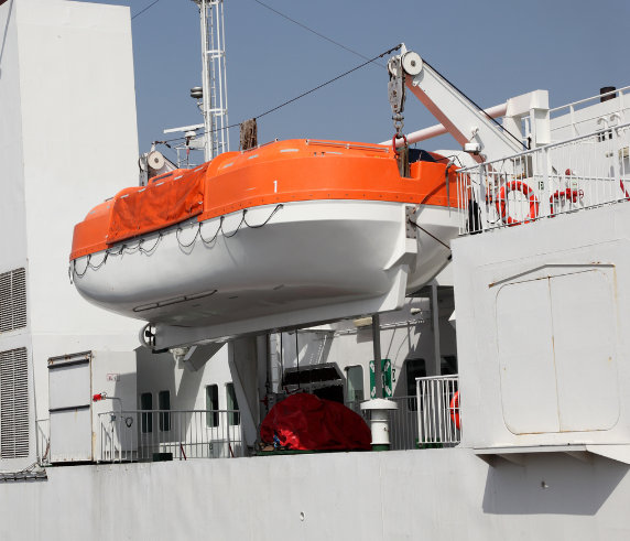 An orange lifeboat is suspended above a white deck by a swing arm davit, which is a type of crane mechanism used for lowering and raising boats on ships. The davit consists of a white metal structure with cables and winches, set against a backdrop of cloudy skies and mountainous terrain.