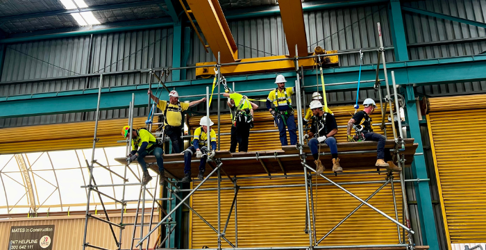 Workers in safety harnesses and helmets working on an industrial scaffolding structure inside a facility, demonstrating the techniques and skills taught in the Scaffolding Intermediate course